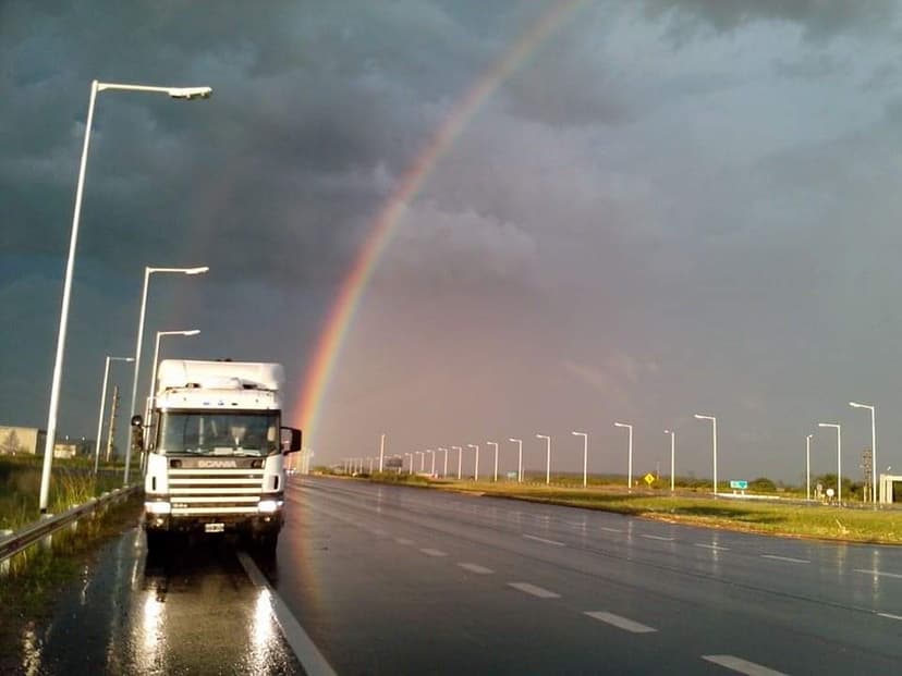 Freight truck parked on a wet road with a rainbow in the sky after a storm.
